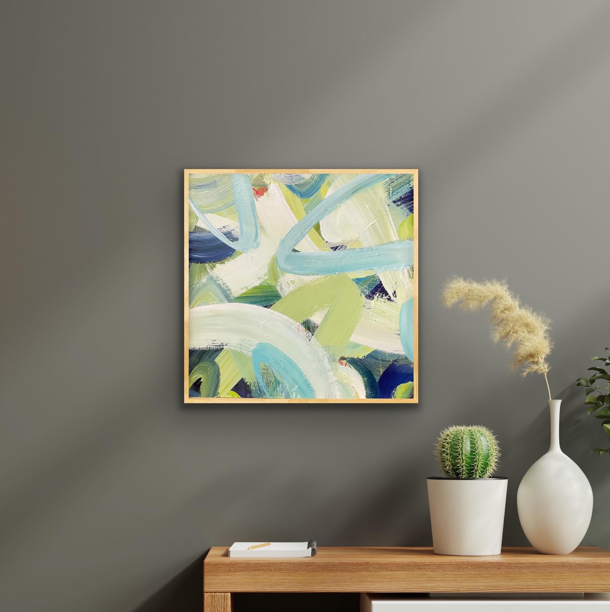 picture of a blue and green abstract painting on a taupe coloured wall above a console table with a cactus on it.