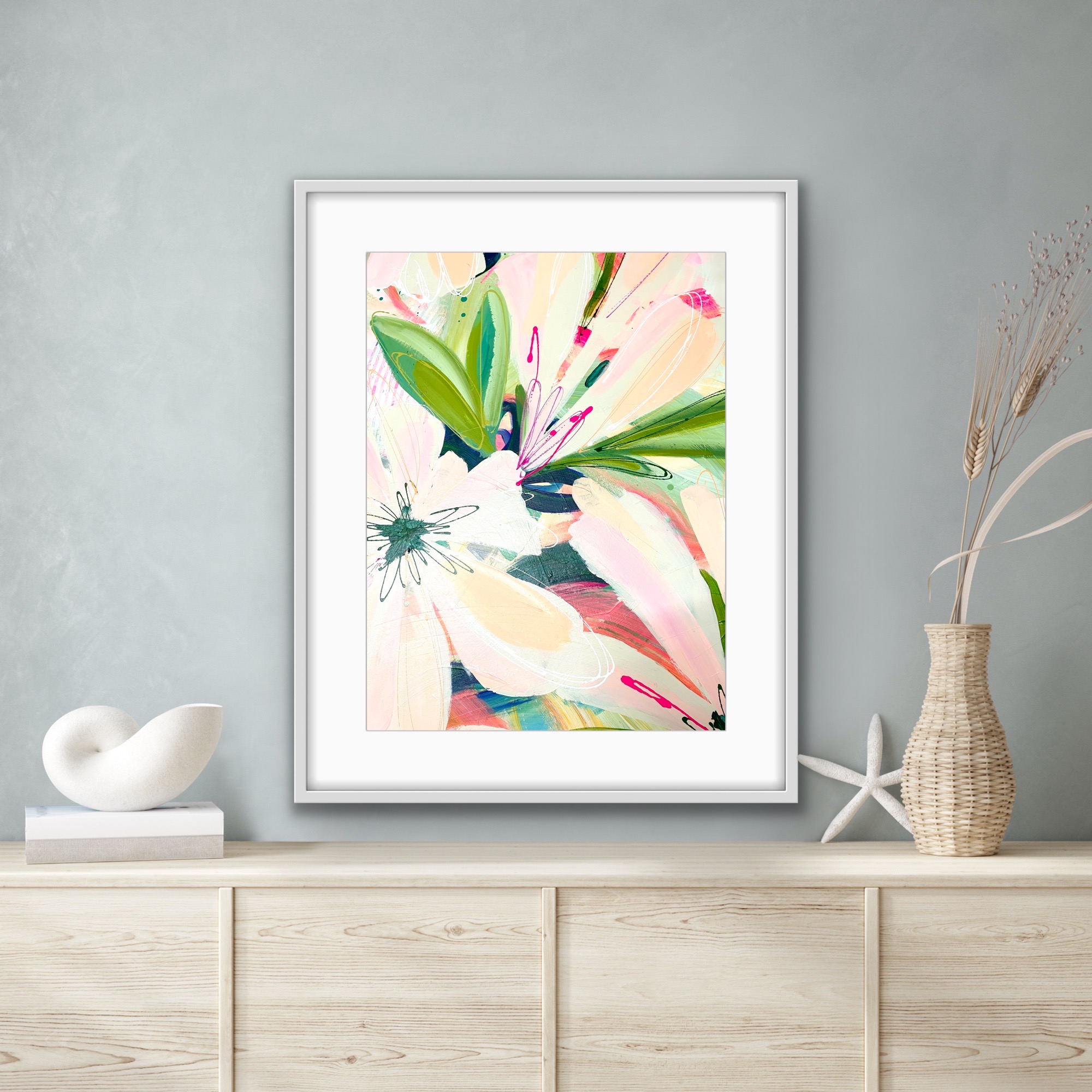 Print of peach and pink tropical flowers, framed and hanging on a light grey wall.